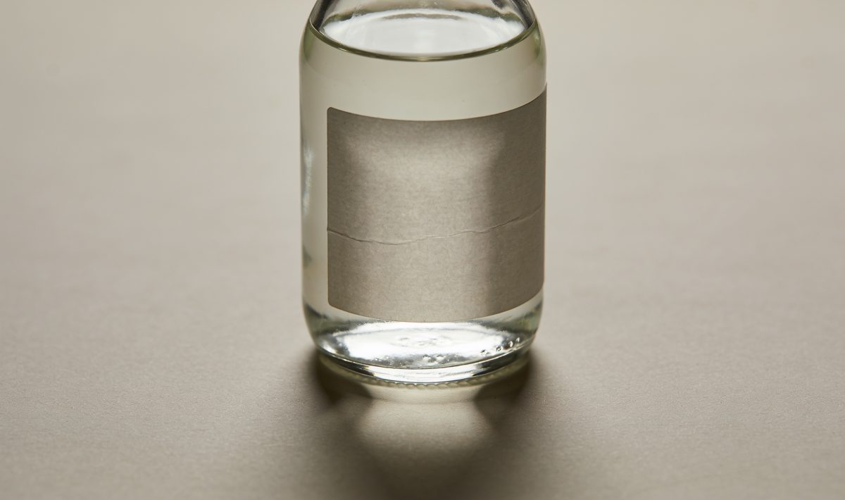 Bouteille de verre contenant liquide translucide, etiquette visible.
