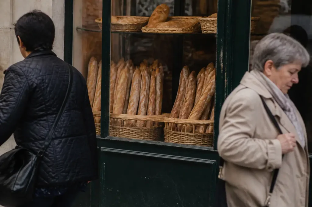Boulangerie avec baguettes en vitrine et passants devant